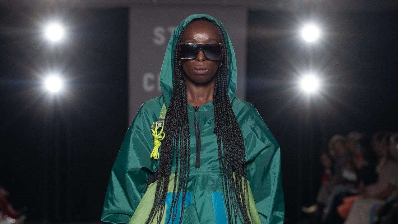 Model Eunice Olumide is pictured on the catwalk wearing sunglasses and a blue and green dress made out of recycled tents.