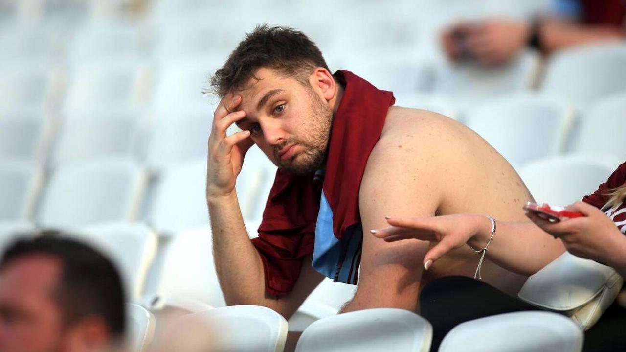A West Ham supporter looks dejected with a hand on his head sat in an almost empty stadium