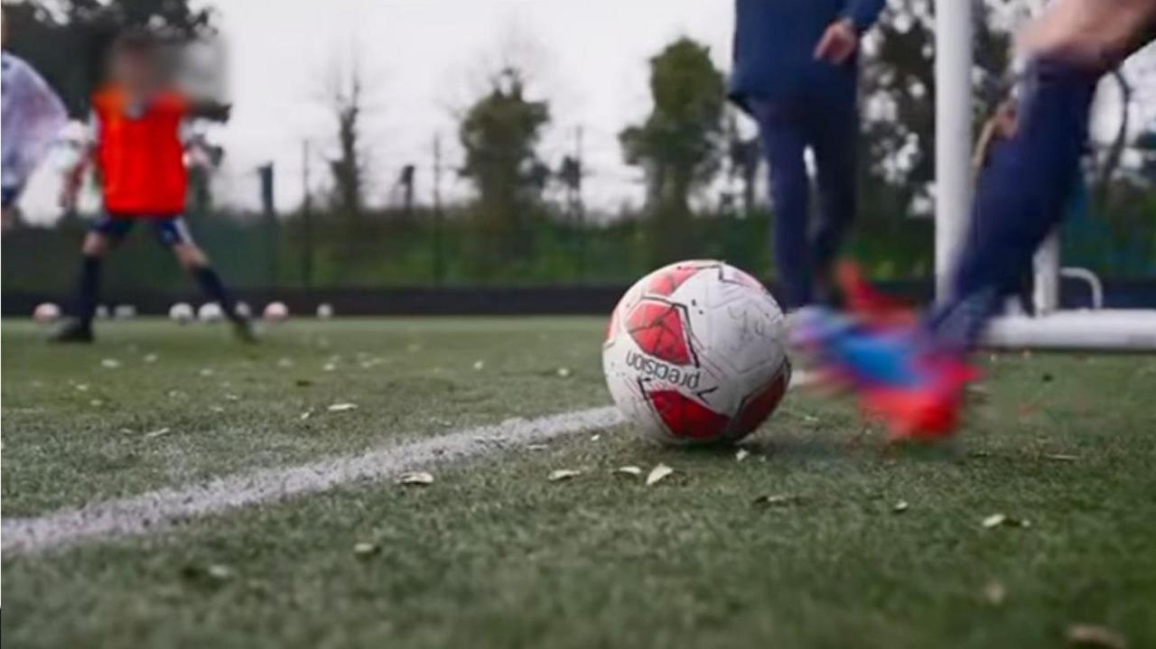 A football about to be kicked on a football field with a number of other anonymous players in the background.