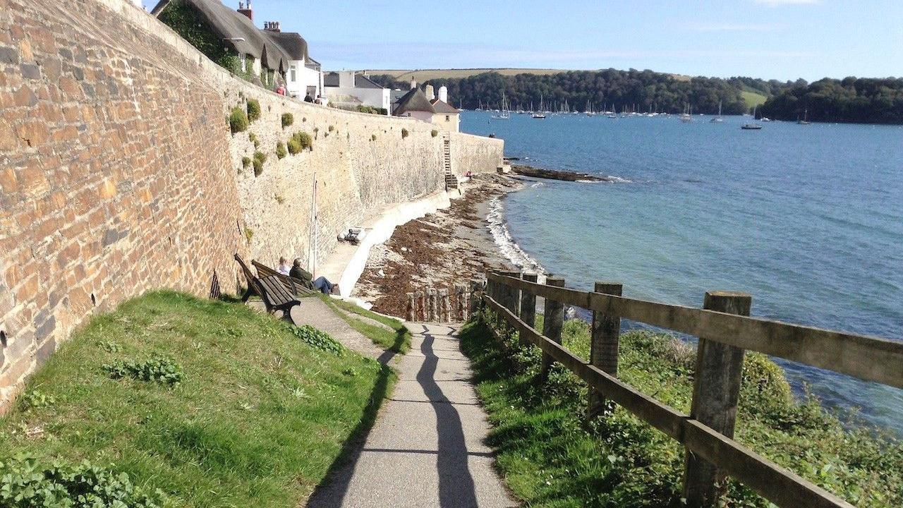 A beach scene with the slipway with benches to sit on the left, the beach in front, and a fence on the right.