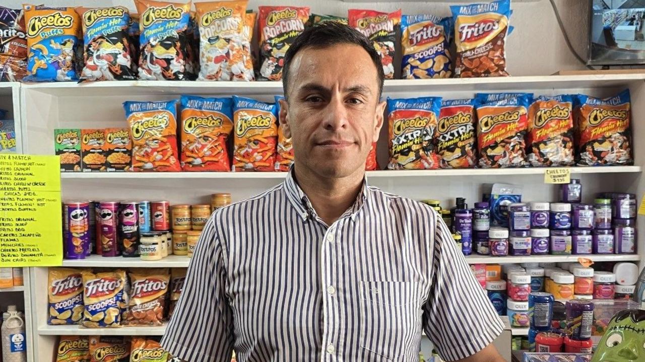 Shop owner Adrian Ramos standing in front on food items on shelves