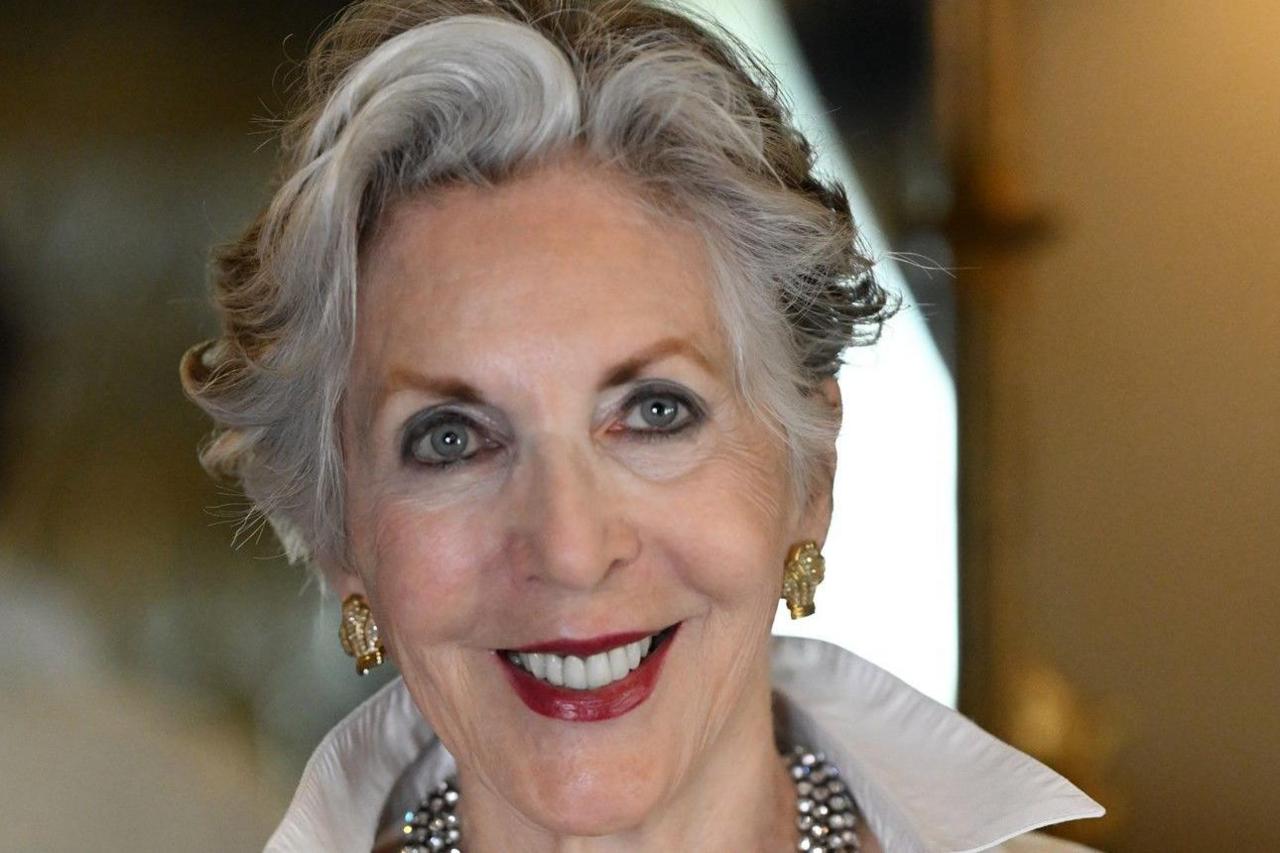 Sherry is smiling at the camera. She has short grey and black hair. She wears a chunk silver necklace and gold earrings.