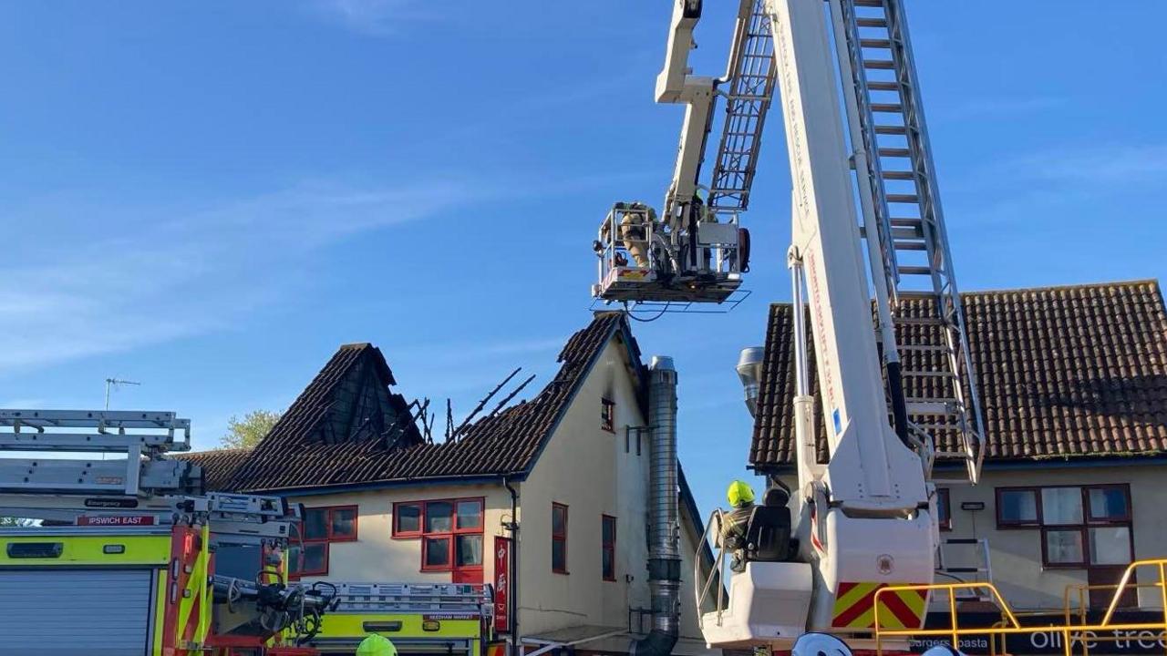 A closer view of the building that has been damaged in a fire. An aerial ladder is in use close to the building.