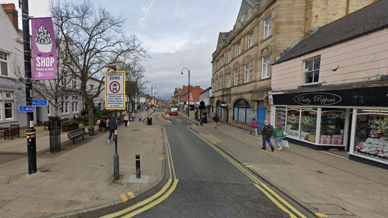 Chester-le-Street's Front Street. A sign marks the road as a pedestrian zone. The road is a single lane with double yellow lines on either side. A number of shops line the high street.