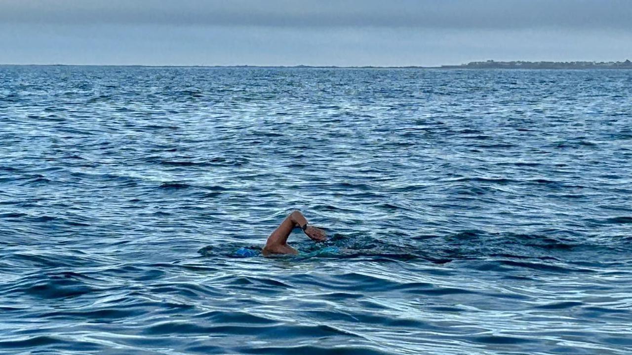 A woman in the open sea water swimming. Skies are grey.
