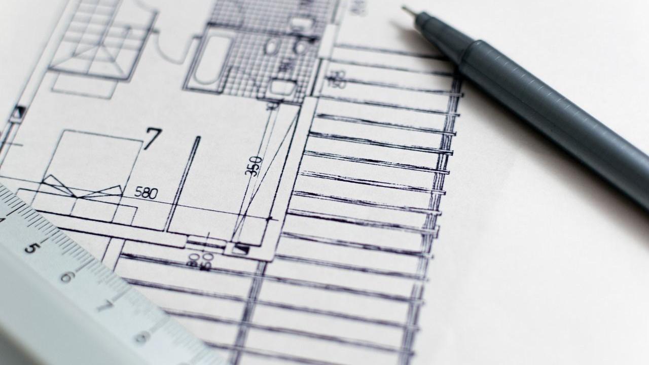 A close-up of a blue print for a property. There is a pen resting on one corner of the drawing and a ruler resting on the other.