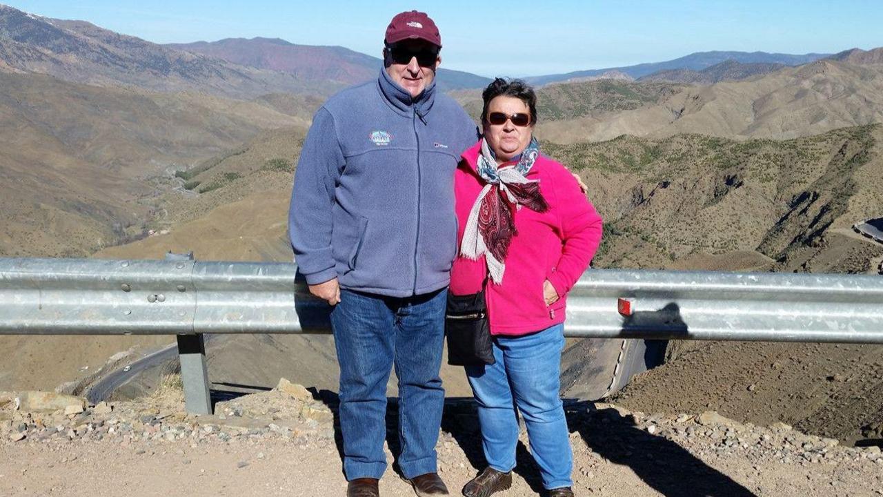 Rodrick Lodge and his wife Pauline standing in front of a mountainous landscape. They are both wearing fleeces and sunglasses and smiling at the camera. 