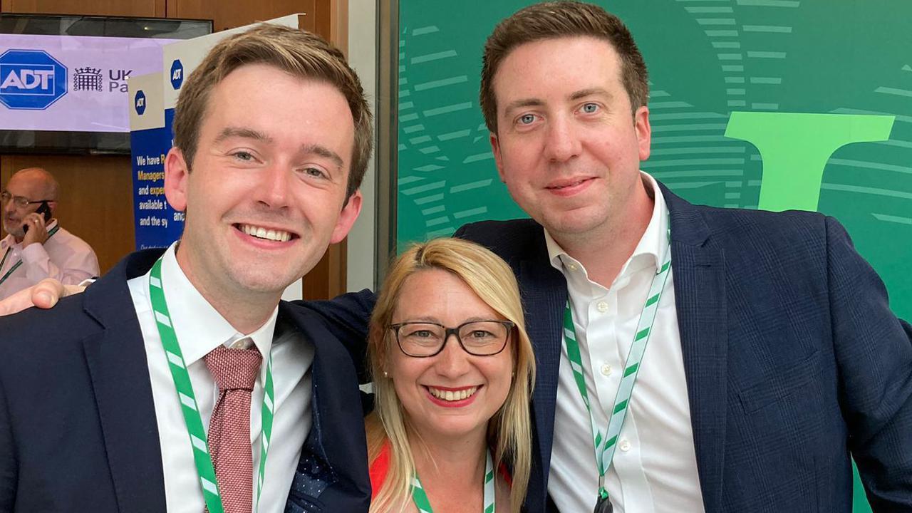 Tom Rutland, Jessica Asato and Liam Conlon smiling as they wear the same green and white striped lanyards