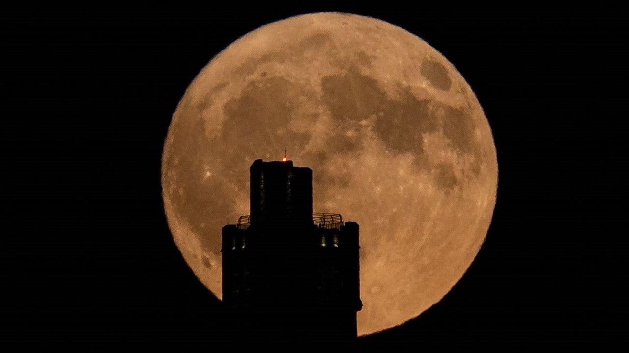 Orange glaze of full Moon rises behind the silhouette of a tower