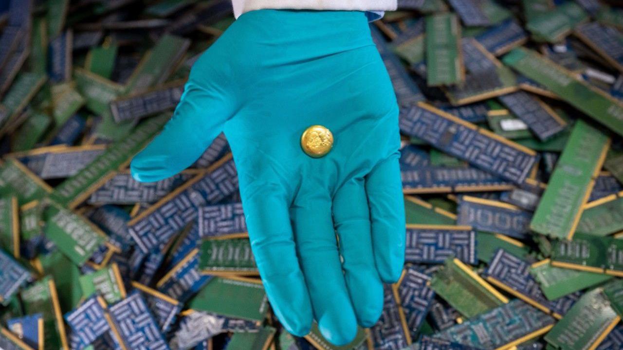 Gloved hand holding a gold nugget above a load of circuit boards