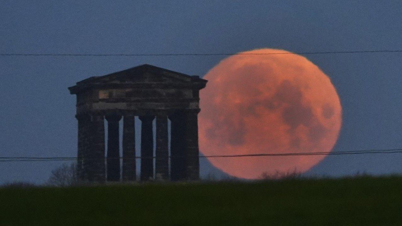 A bright orangey red Worm Moon sits to the right of Penshaw Monument, near Sunderland
