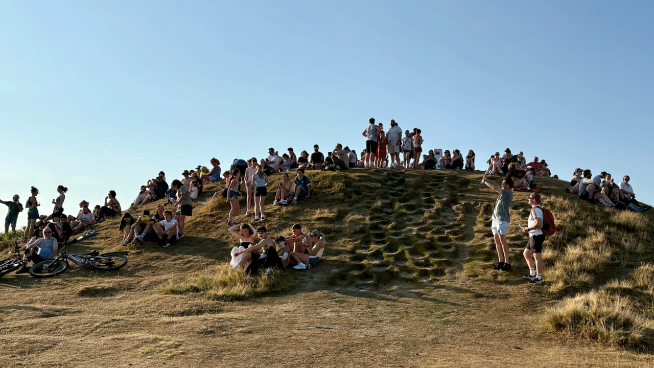 A large group of people sit and stand on a hillside looking skywards