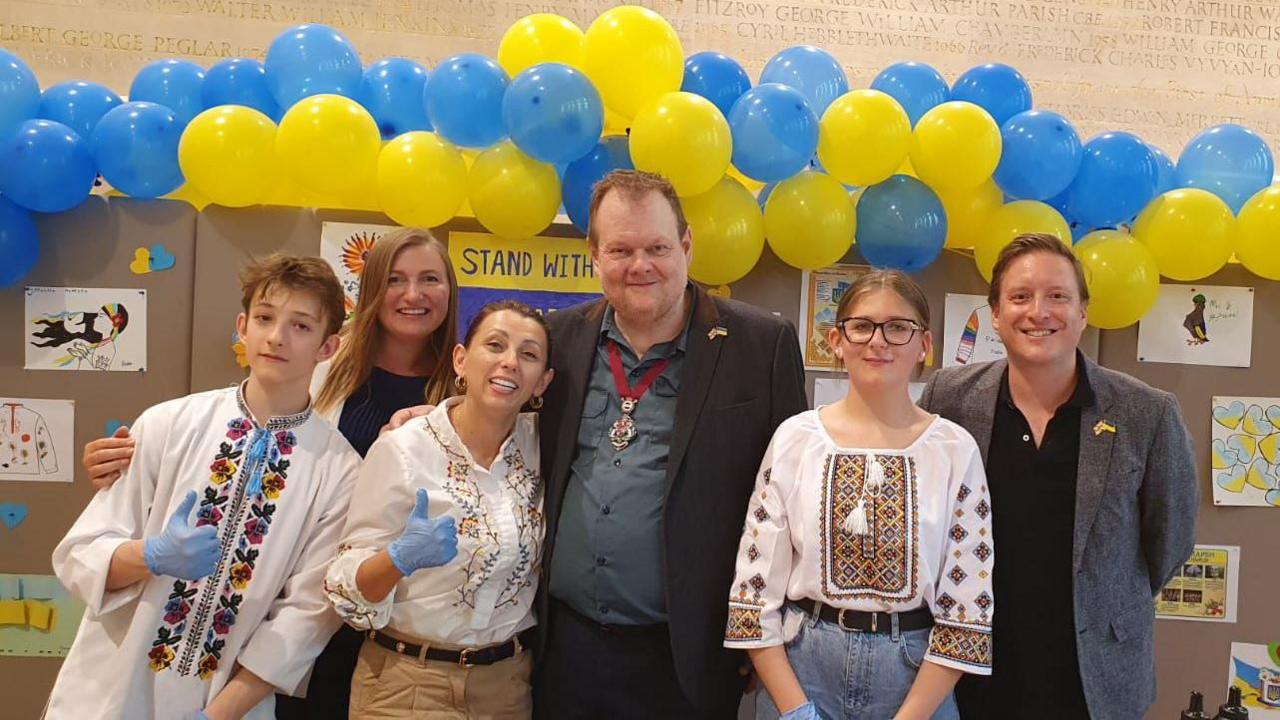 Six people posing for a photo under blue and yellow balloons