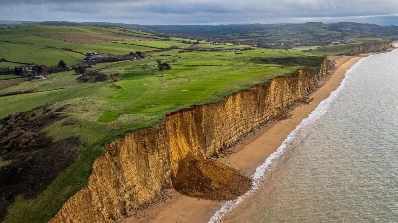 A drone image of a collapsed section of sea cliff which is completely blocking the beach below