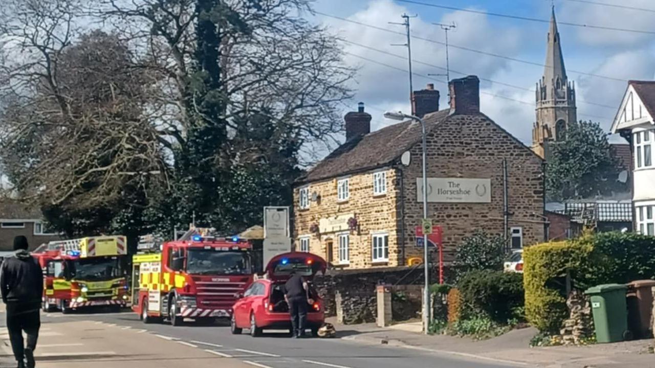 Two fire engines and a red response car outside a brick pub, which is next to a residential road. The pub is two-storey and has cream bricks.