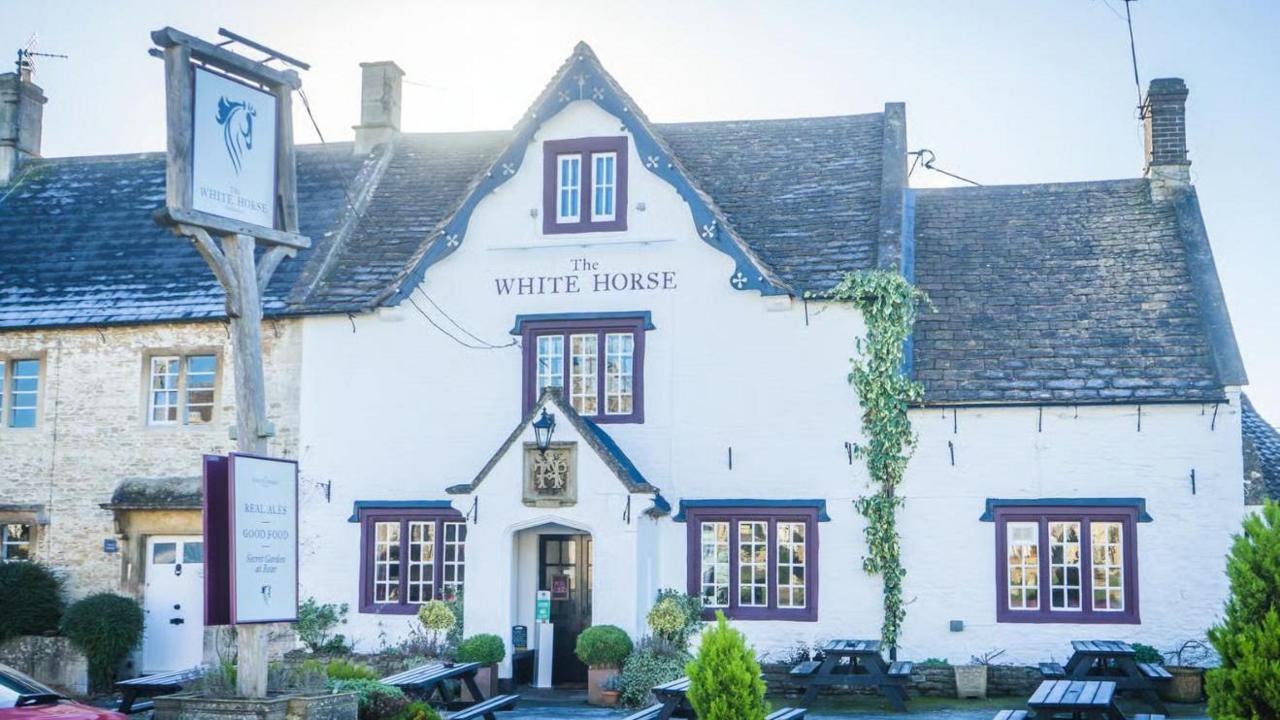 The White Horse Inn from the front. It is a white building with red window frames and picnic benches outside.
