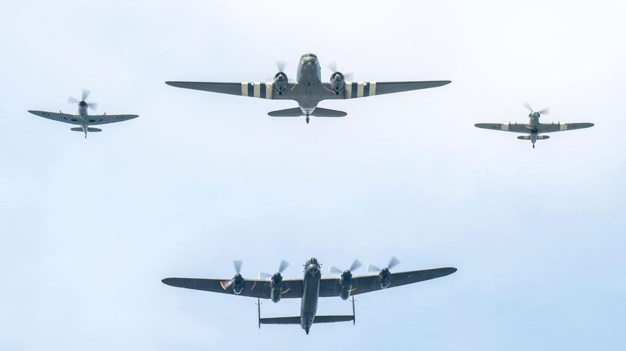 Silhouettes of four aircraft, two large two small on a pale blue sky. The largest aircraft has four rotors.