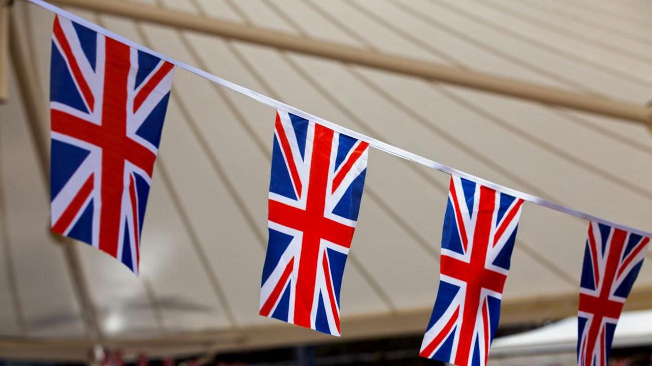 Union Jack flags hanging across a bunting with an awning in the background.