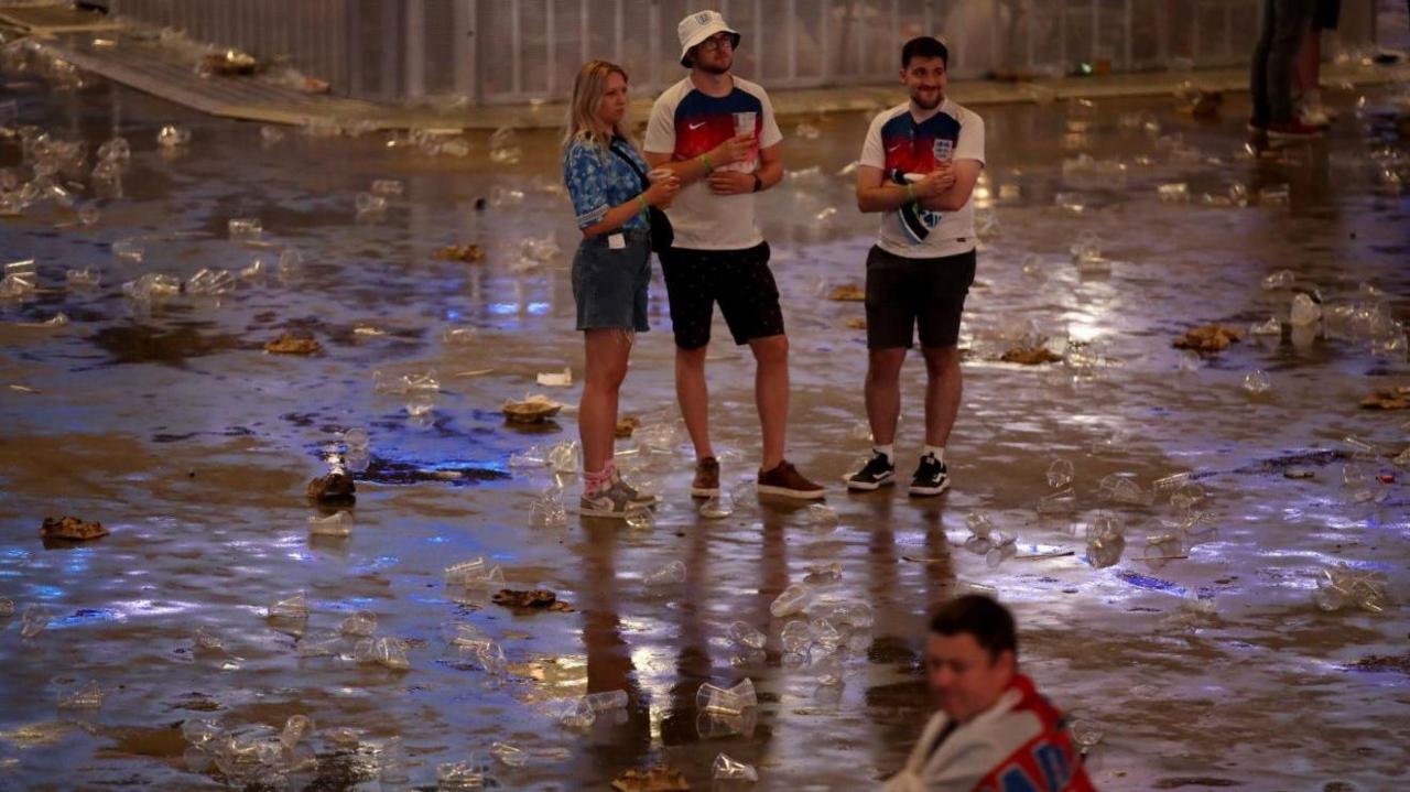 Four England fans stand in the O2 arena surrounded by empty beer cups