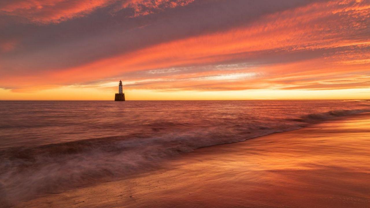 A beach at sunrise with a  lighthouse in the background