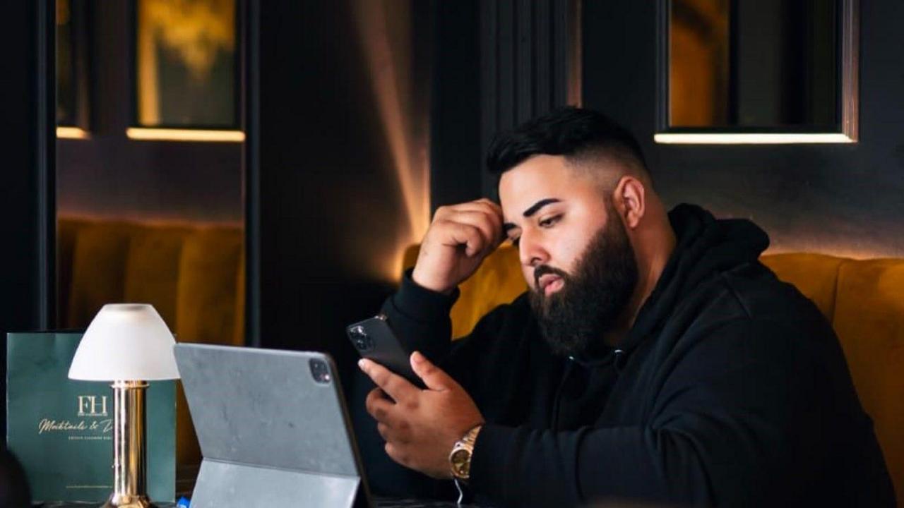 Mohammed Sarnwal wearing a black hoodie looking in to his iPad and phone, leaning his head on his hand.