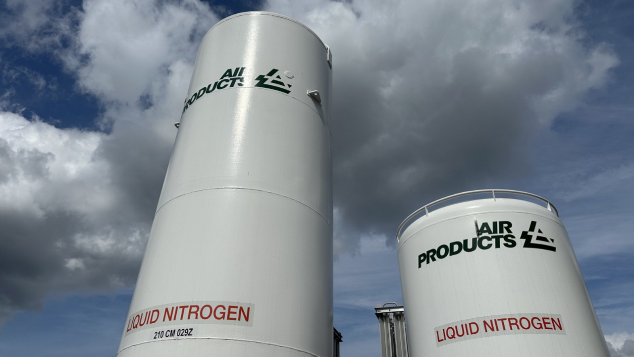 Two metal cylindrical towers can be seen, labelled liquid nitrogen. They are white and different heights and there is blue sky with clouds above them. 
