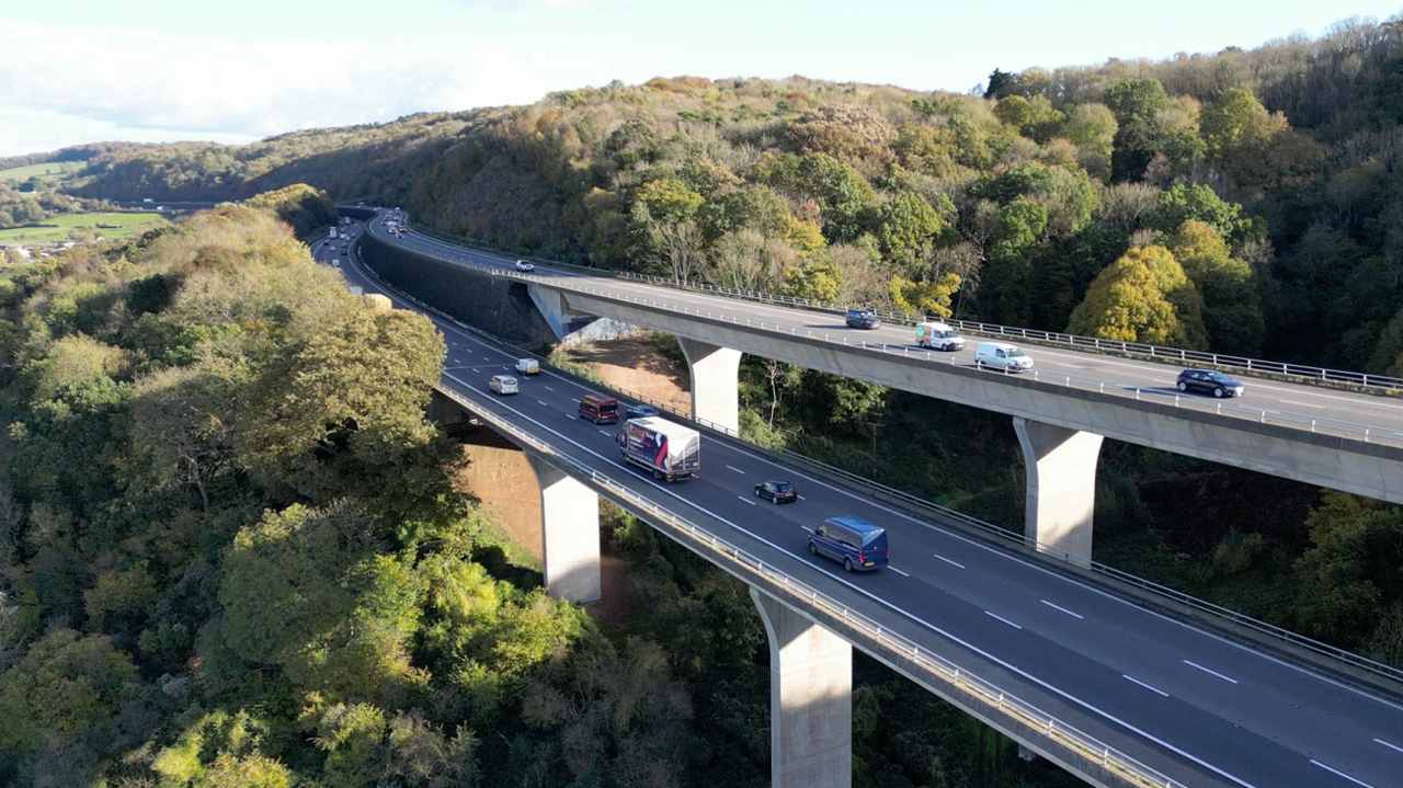 The split section of the M5 south of Bristol is seen from a drone. The image is taken in the daytime on a sunny day, and there are cars and lorries on all carriageways