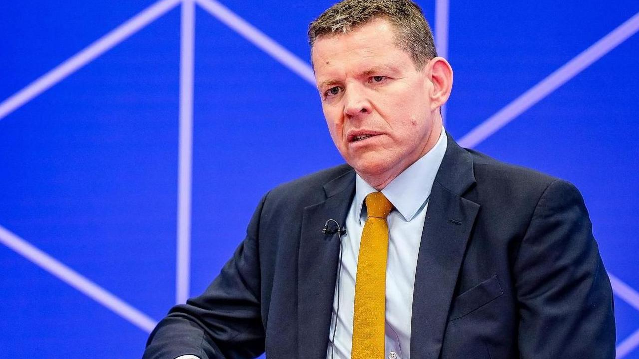 Rhun ap Iorwerth with a serious expression in a television studio wearing a suit and yellow tie