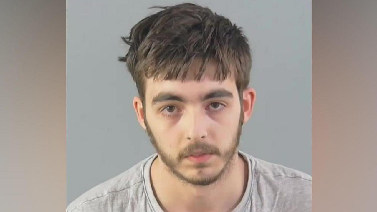 Carlo Tritta, who is wearing a grey jumper, is staring directly at the camera in this custody mugshot. He has straight, light brown hair and a thin beard.