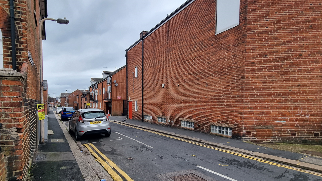 A view of the junction between Goldsmid Road and Russell Street. There are two red brick buildings either side of a narrow street with terraced housing up either side.