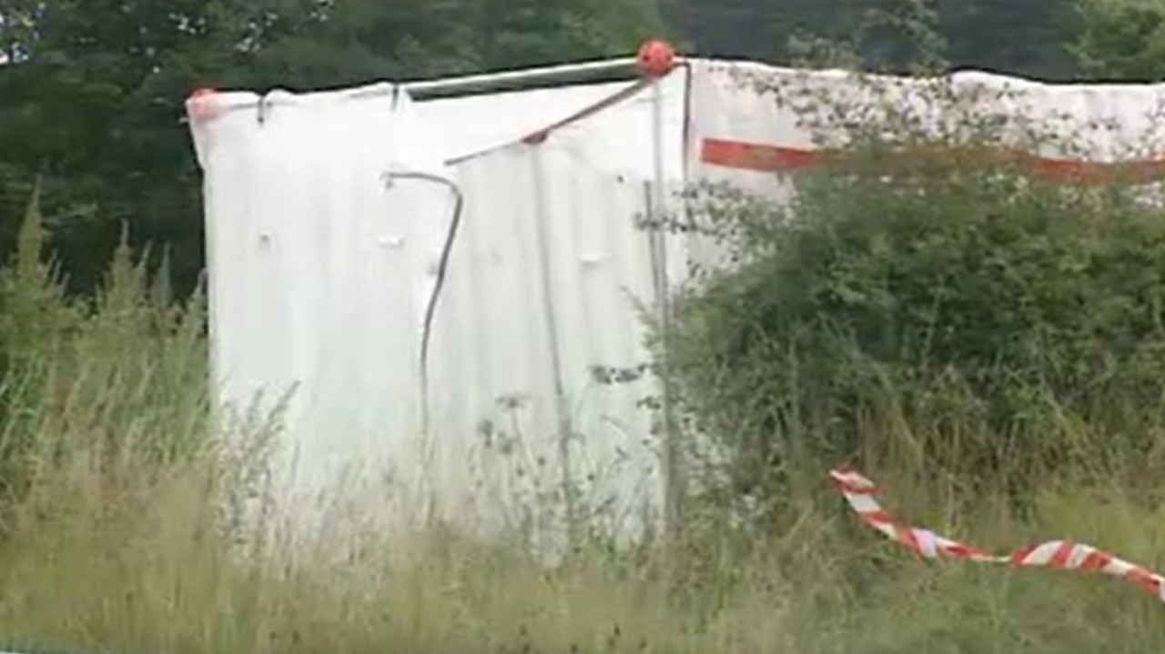 A white forensic tent stands in an overgrown field