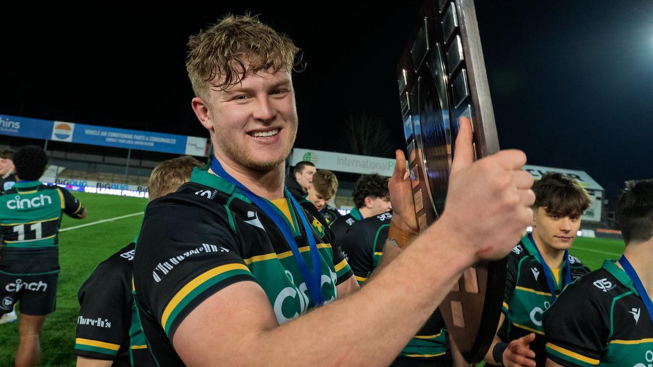 Northampton captain Jack Lawrence, wearing a green, black and gold rugby kit and with a medal around his neck, holds the Under-18 academy trophy
