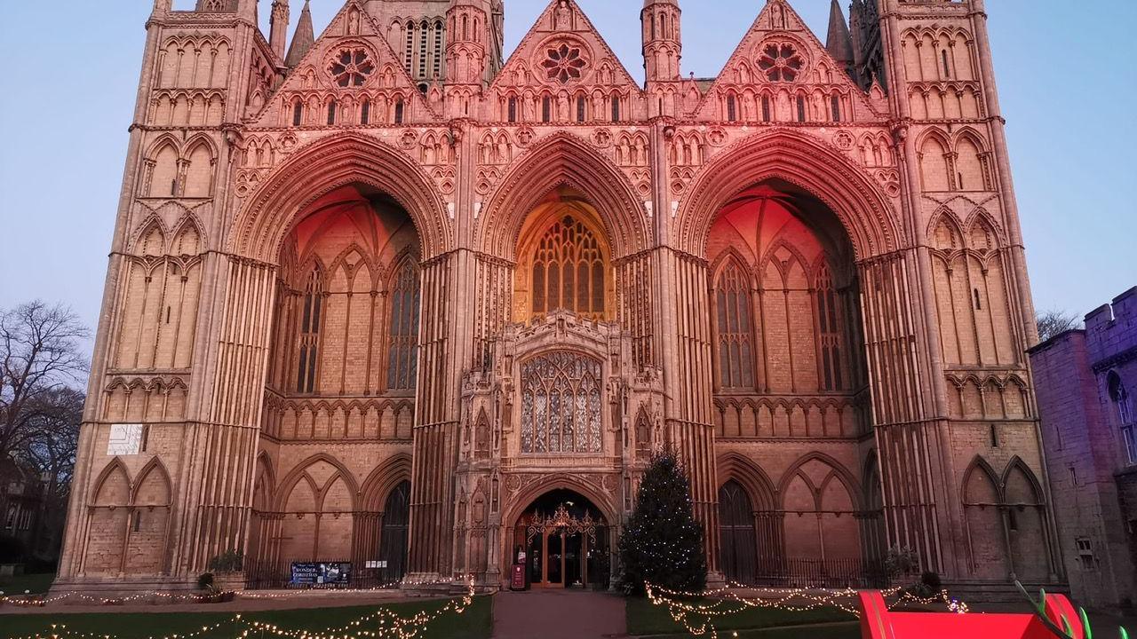 Picture of Peterborough Cathedral - lit up in a faint red colour with fairy lights placed on the lawn in front.