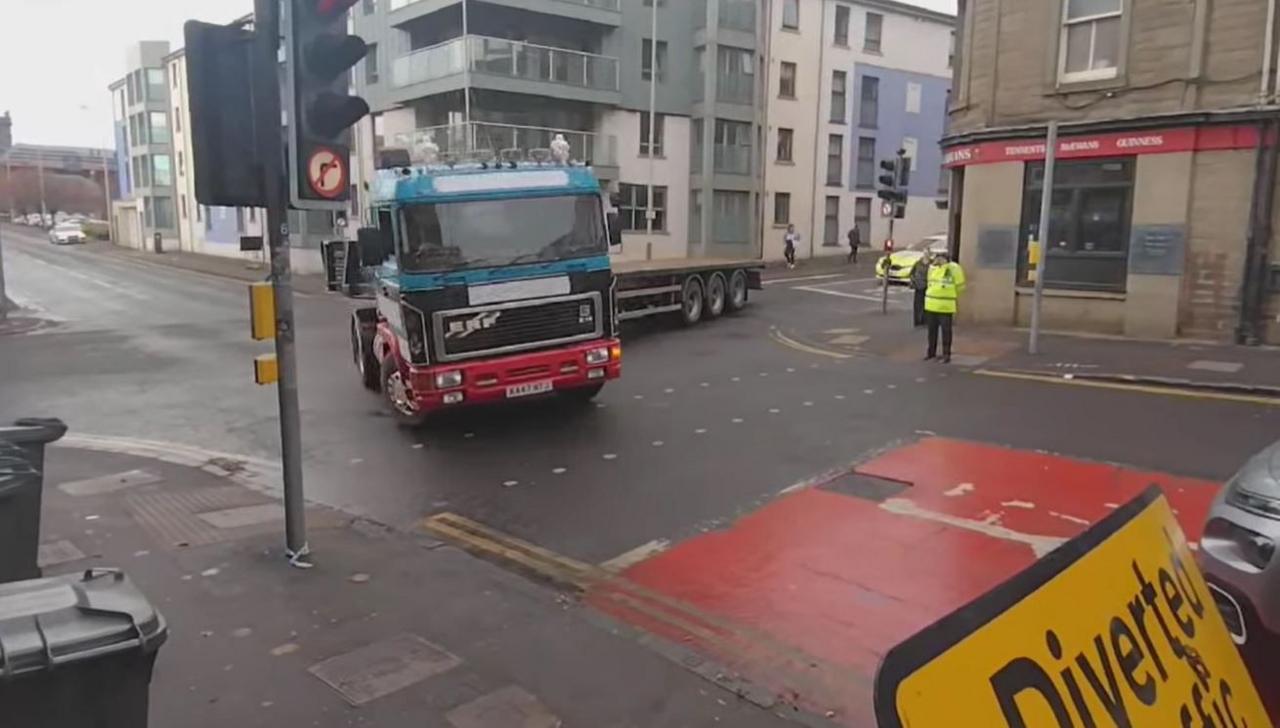 An HGV turns a corner onto a street watched by a police officer