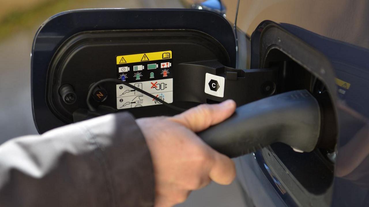 A hand holding a black electric car charging cable, plugged into the charging point of a car