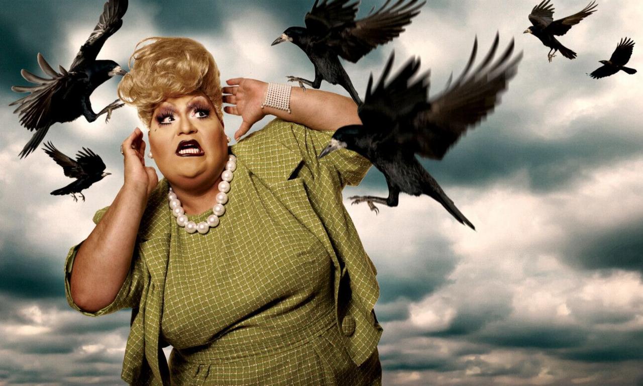 A drag queen in a checkered green dress is attacked by super-imposed crows