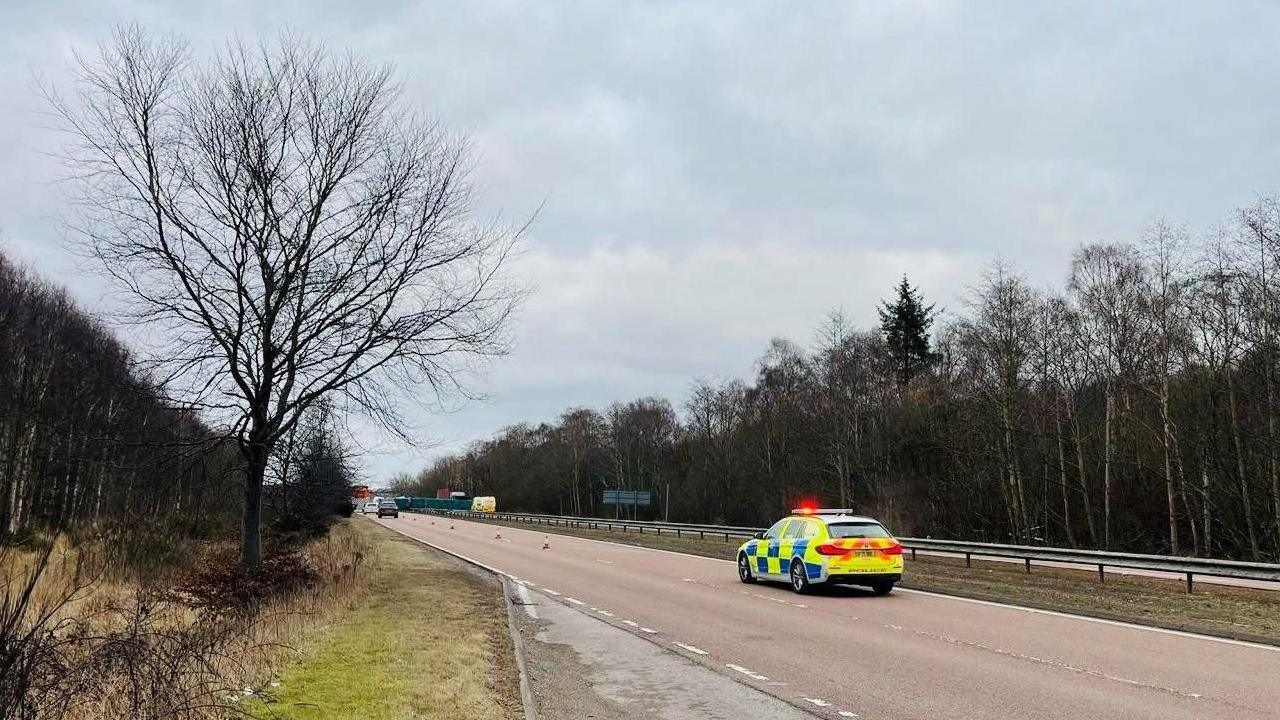 Police car on a dual carriageway with an accident scene in the distance.