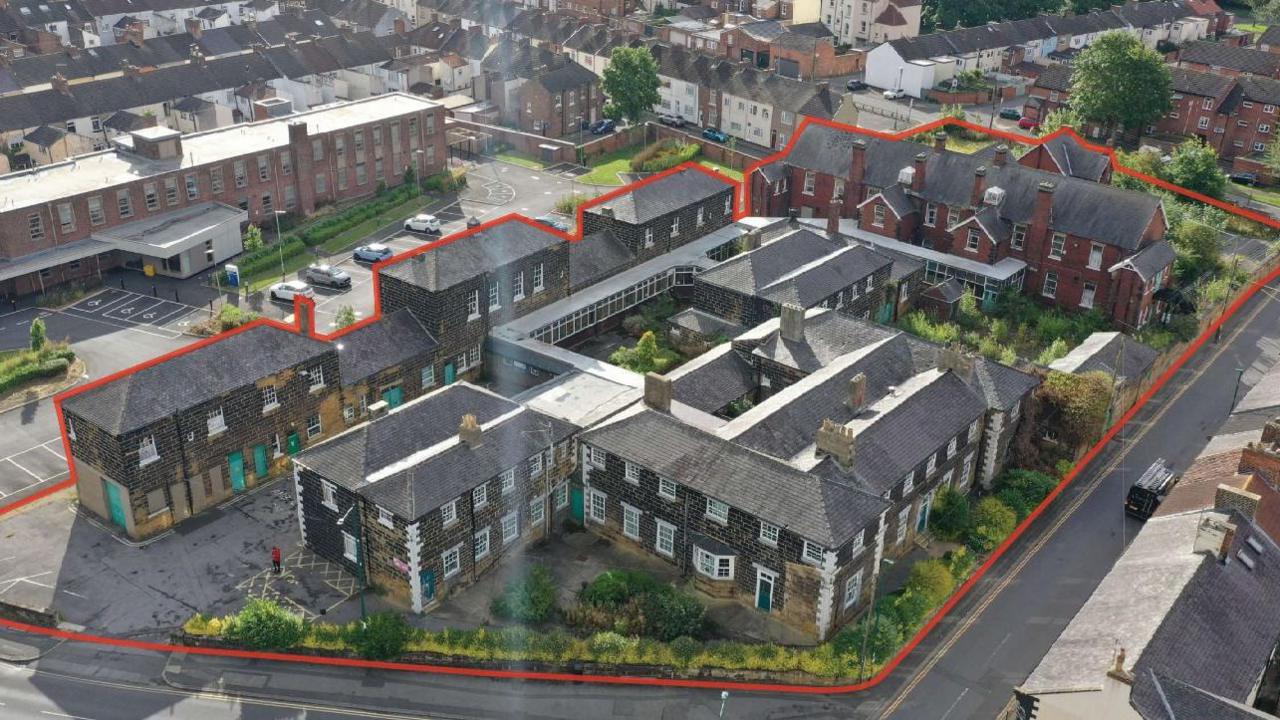 A drone shot of the site with the boundary marked in red. The building is made of old grey brick. The hospital site looks similar to a collection of terraced houses.