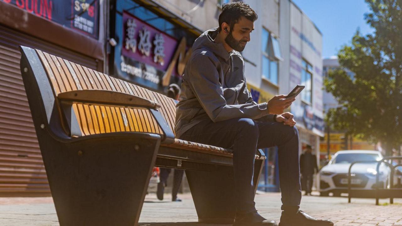 A man listening to an audio story on a bench in Luton