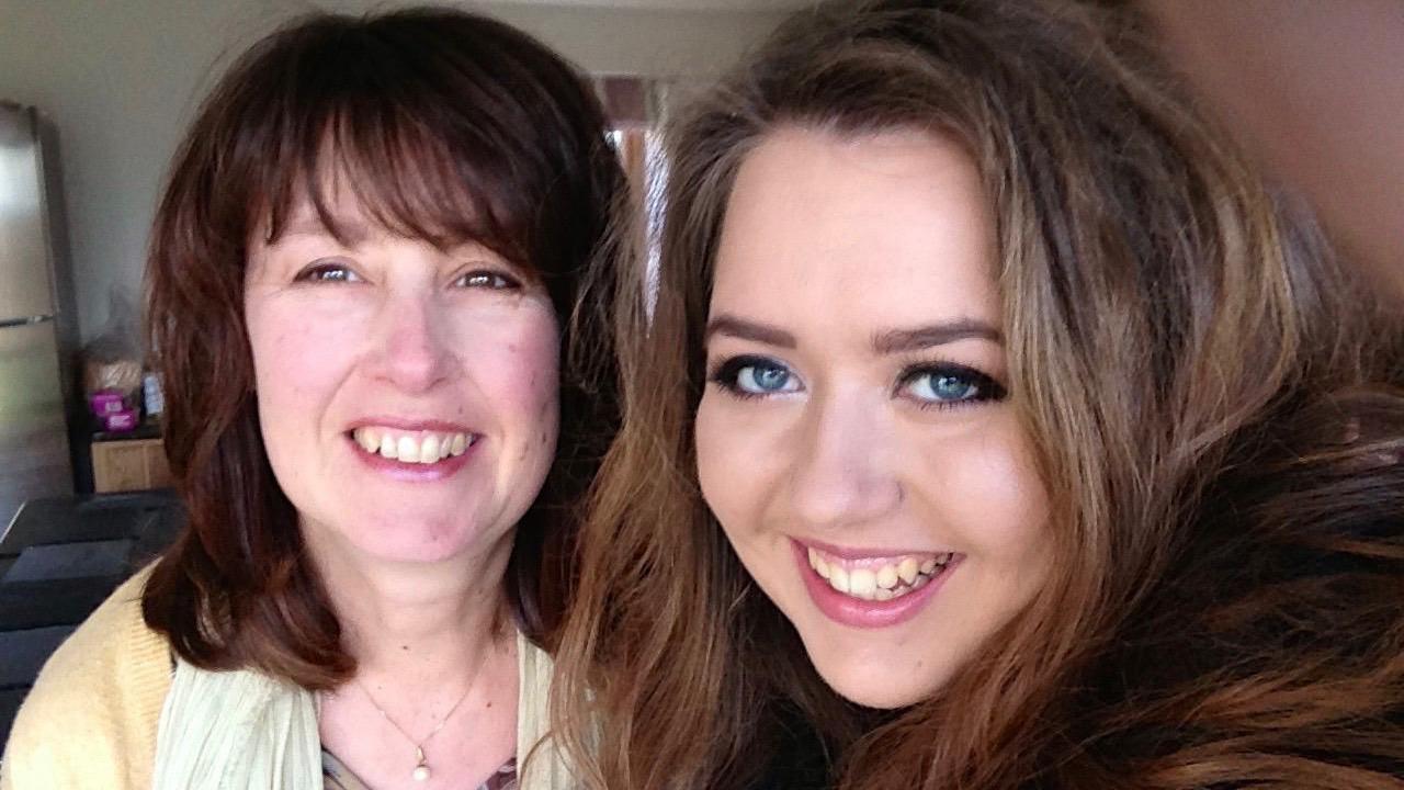 A smiling woman with long dark hair next to a younger woman, also smiling and with long long brown hair