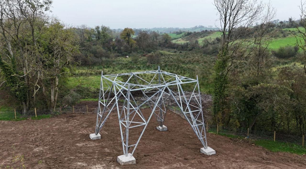 Four base legs of an metal electrical pylon built in a mud field.