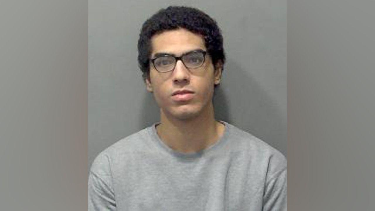 Nicholas Prosper, who has dark hair and dark glasses, staring into the camera for a police custody image. He is wearing a grey sweatshirt. 