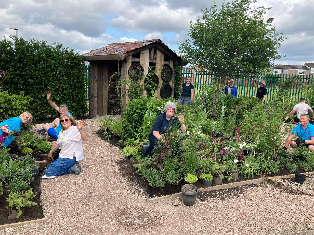 Volunteers are in among the plant son their knees at different parts of the garden, and wave to the person taking the phot.