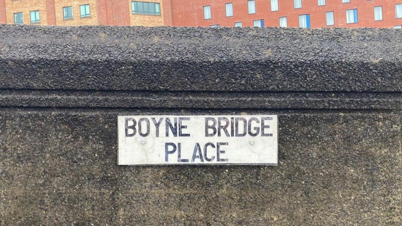 Road sign reading Boyne Bridge Place in black writing on a white background, placed on the concrete bridge