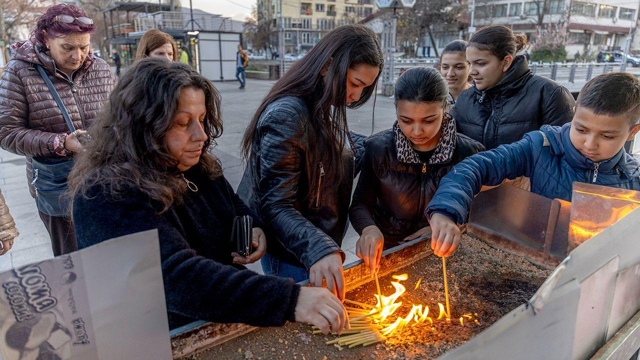 A group of women and younger children burn incense sticks at a vigil for the victims in a square in Kocani on Sunday