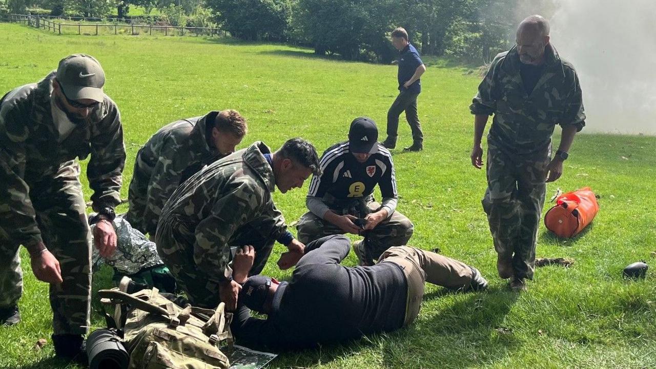 A group including Willy Caballero (left), Aaron Ramsey (second right) and Luke Williams (right) tend to a casualty during a military training exercise as part of the FAW's Uefa pro licence course