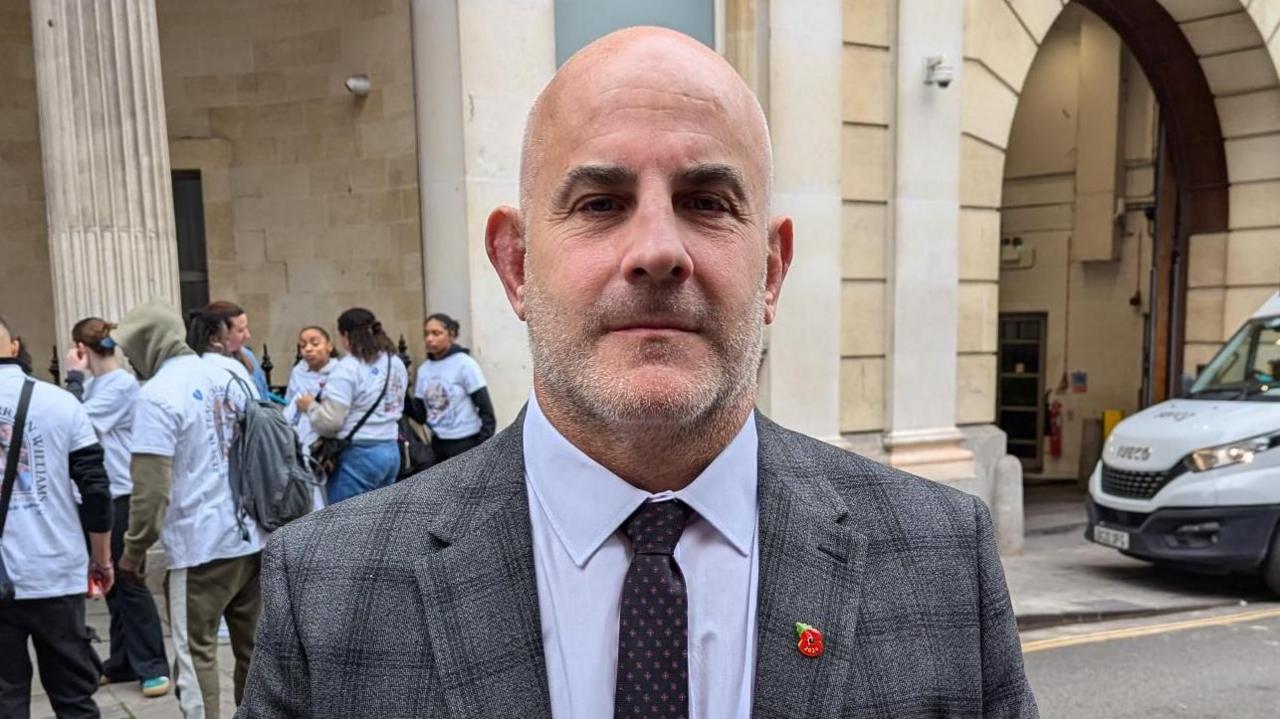 Neil Meade, pictured outside of court. He is wearing a grey suit and a light grey/blue shirt with  dark tie and a small poppy badge. 