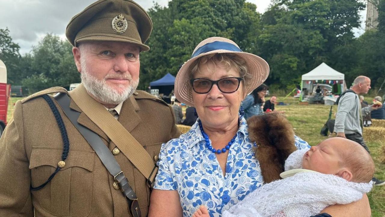 Husband and wife Angela and Phill dressed up in 40s wear with a pretend doll.