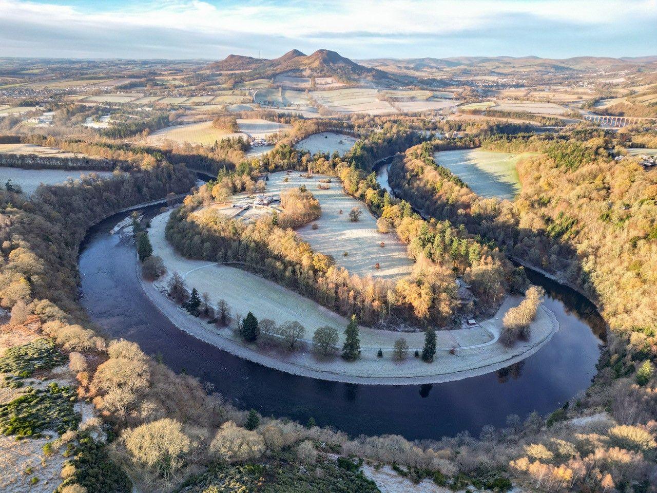 An aerial view of a bend in a river with trees on the shoreline and frosty hills in the distance