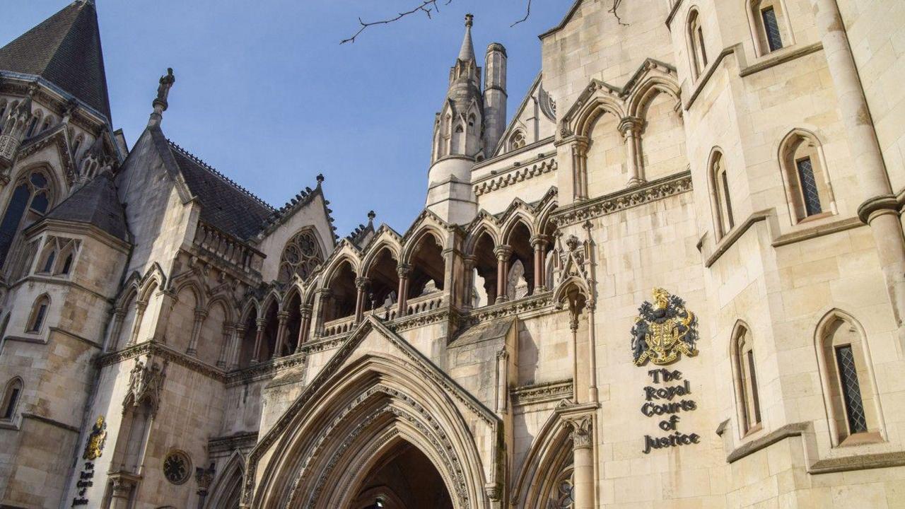 Outside shot of The Royal Courts of Justice showing the front of the building., which is large and made from pale-coloured stone. There are numerous windows, towers and archways, and the words The Royal Courts of Justice below a coat of arms.